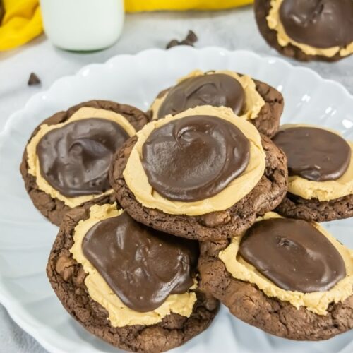 A white plate holding several chocolate cookies topped with a layer of peanut butter and chocolate frosting.