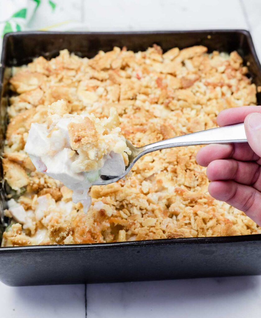 A hand holding a spoon full of Cheesy Ritz Cracker Chicken Casserole.