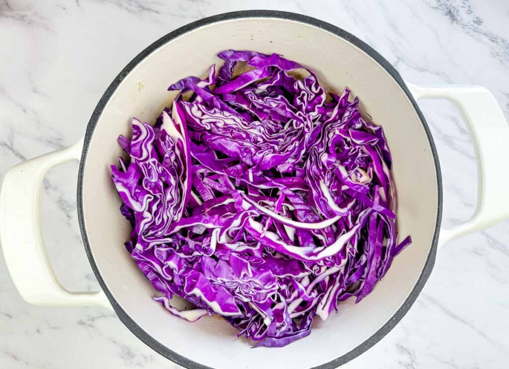 Sliced purple cabbage in a white pot on a marble countertop, ready to be cooked.