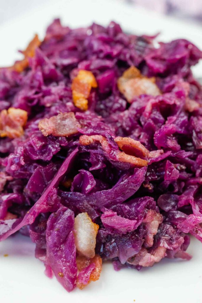 Close-up of cooked red cabbage mixed with pieces of bacon on a white plate.