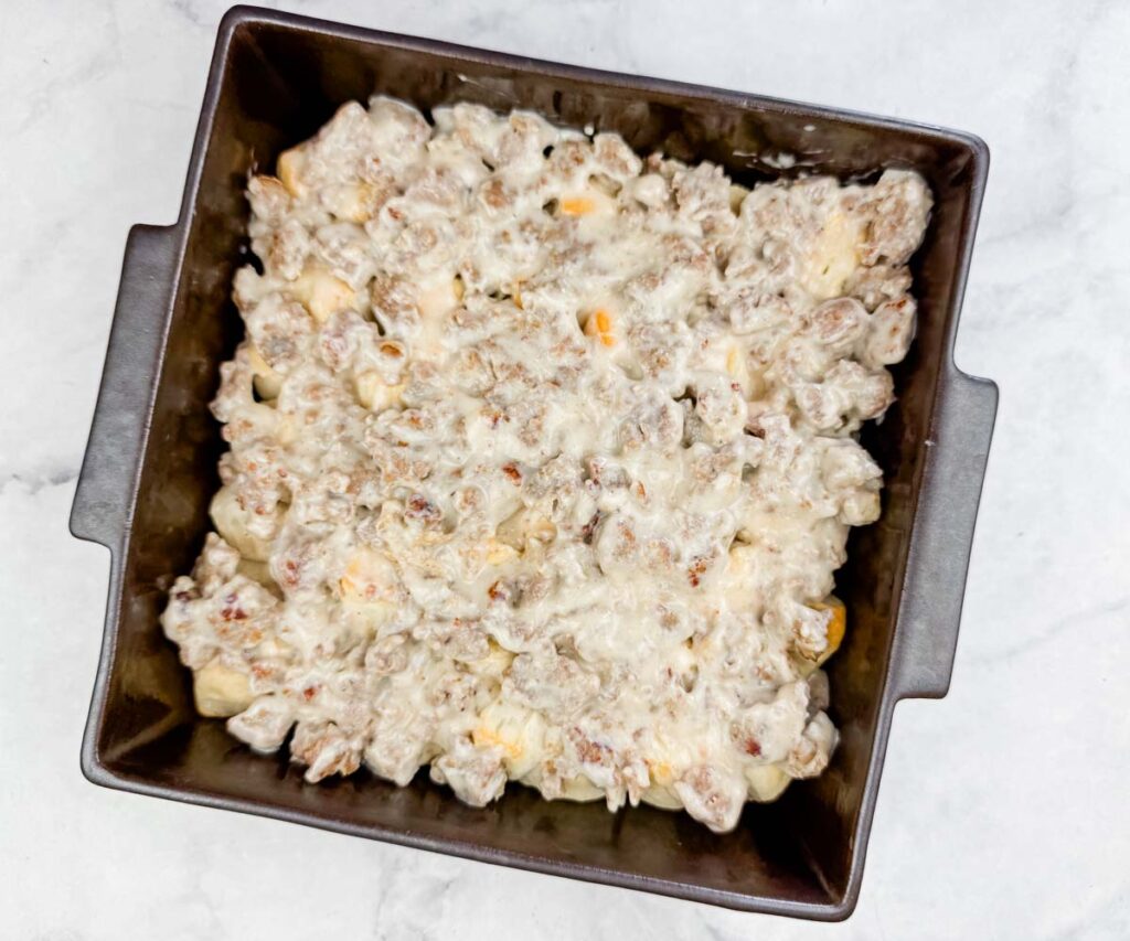 A square metal baking pan filled with a baked casserole made of ground meat and melted cheese on a light marble surface.
