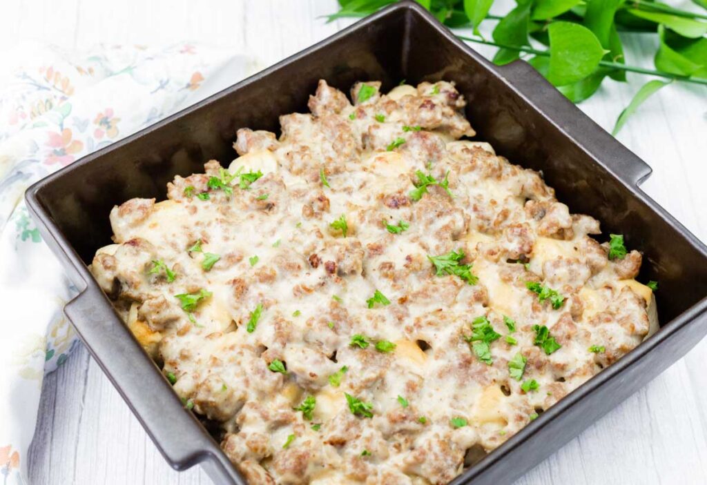A square baking dish filled with a baked casserole topped with ground meat, creamy sauce, and chopped parsley.