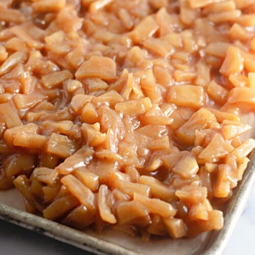 A baking tray filled with a layer of chopped apples coated in a cinnamon-sugar mixture.
