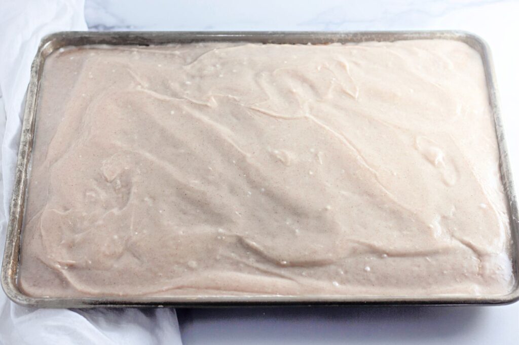A rectangular metal baking pan filled with an even layer of light brown batter on a white surface.