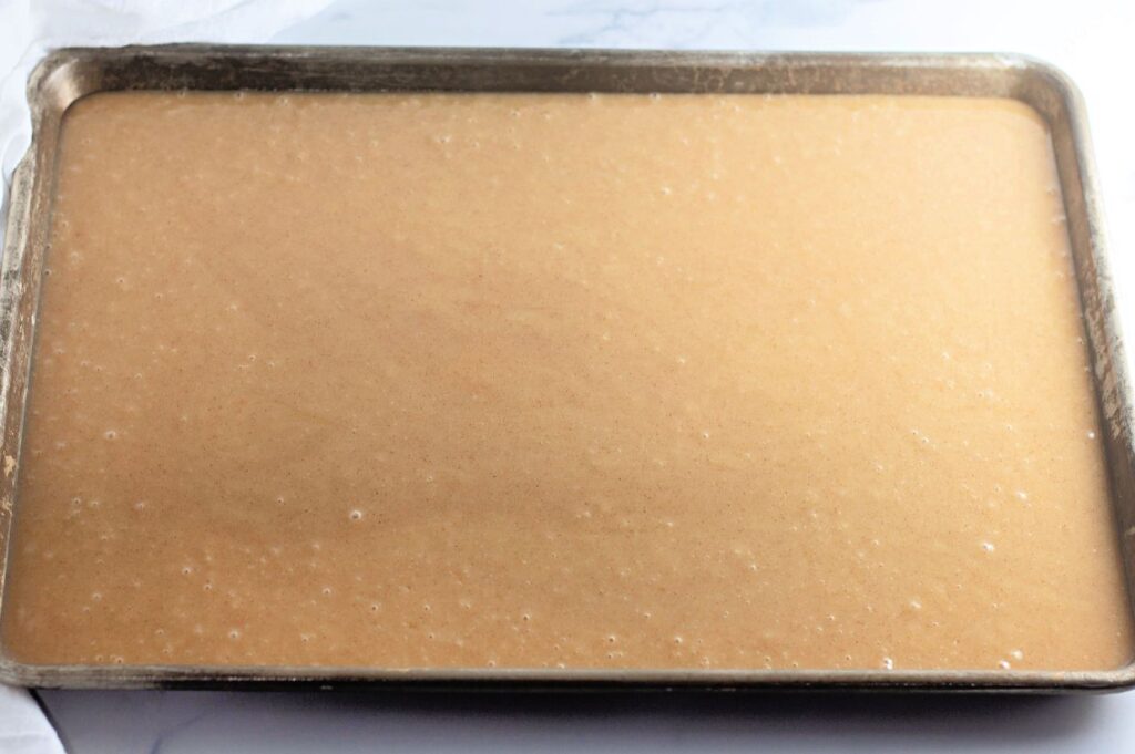 A baking sheet filled with light brown cake batter, evenly spread and ready to be baked.