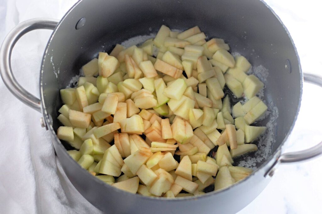 Chopped apples in a large pot, ready to be cooked, with visible sugar on the bottom.