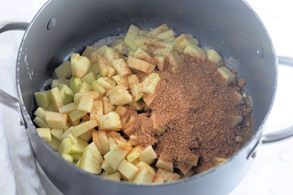Chopped apples and a mound of brown sugar are in a large pot, ready to be cooked.