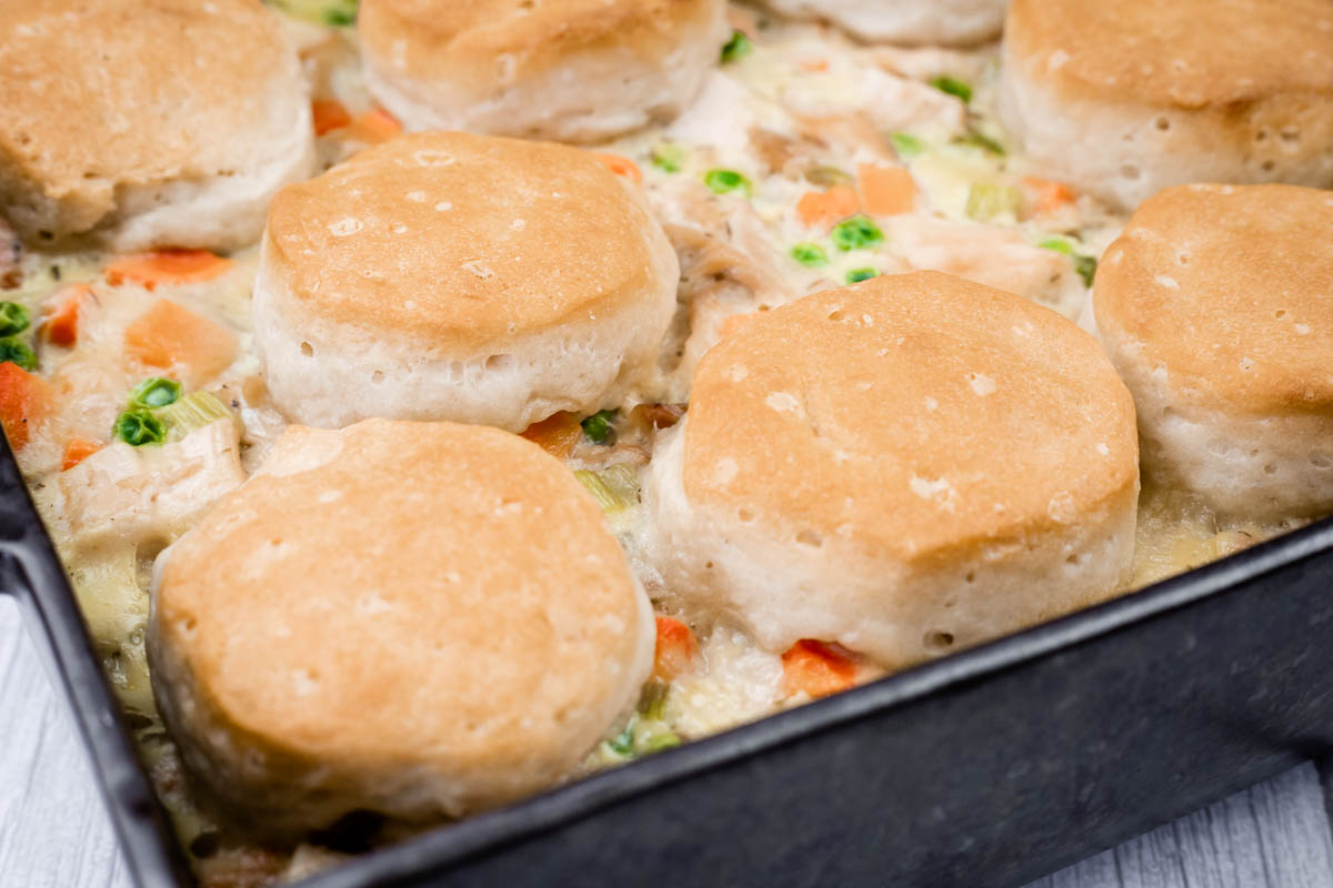 A baking dish filled with creamy chicken and vegetable casserole, topped with golden brown biscuits.