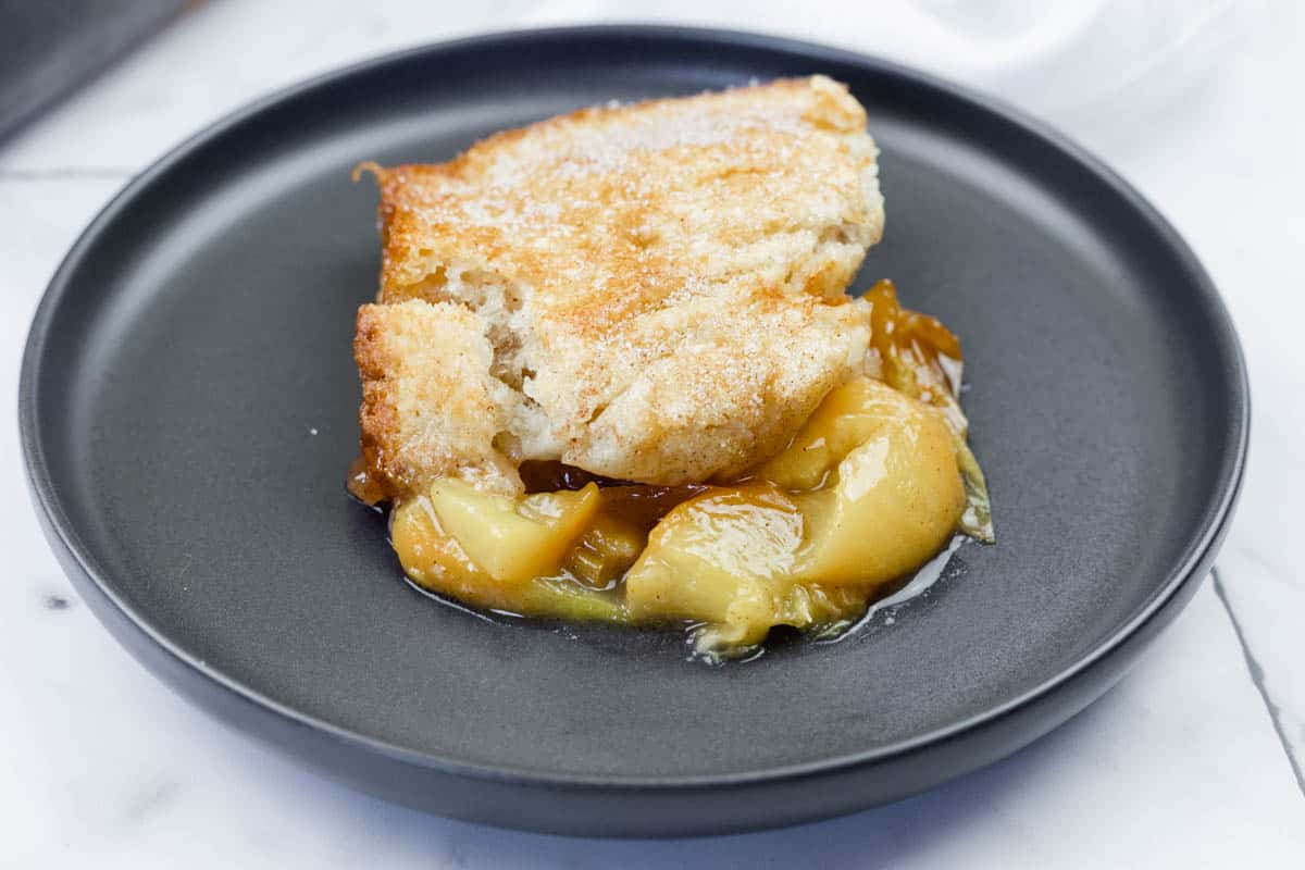 A serving of peach cobbler with a golden crust and peach filling on a black plate.