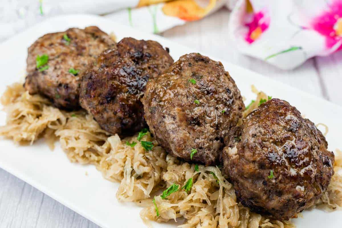 Four browned meat patties are served on a bed of shredded cooked cabbage on a white rectangular plate.
