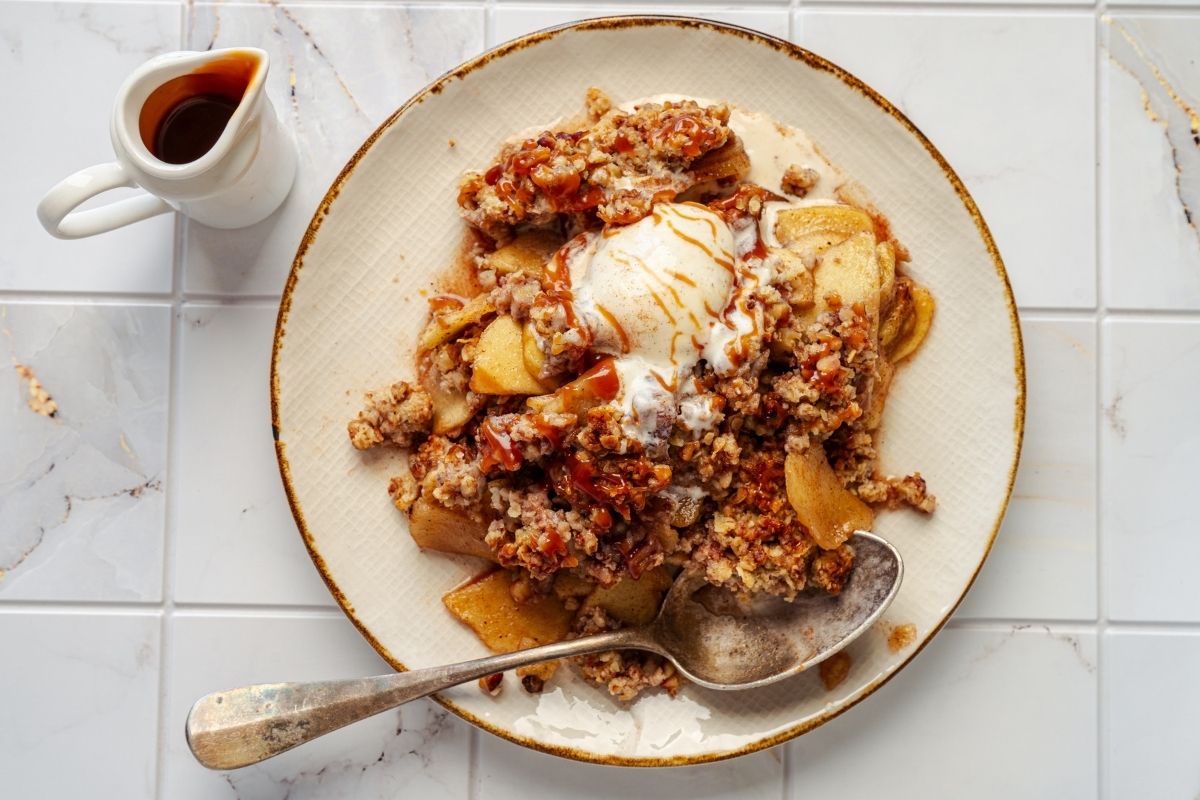 A plate of Classic Apple Crisp with a scoop of vanilla ice cream, served with a spoon.