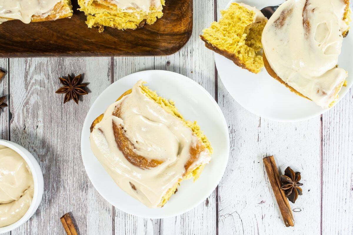 Homemade cinnamon rolls with cream cheese frosting on wooden serving board.