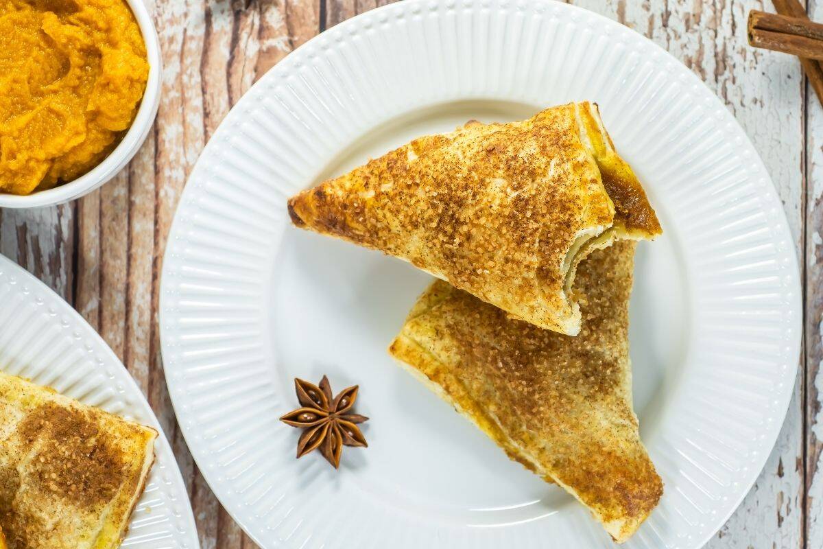Pumpkin turnovers on a white plate, golden brown with spiced sugar topping and pumpkin filling peeking through.