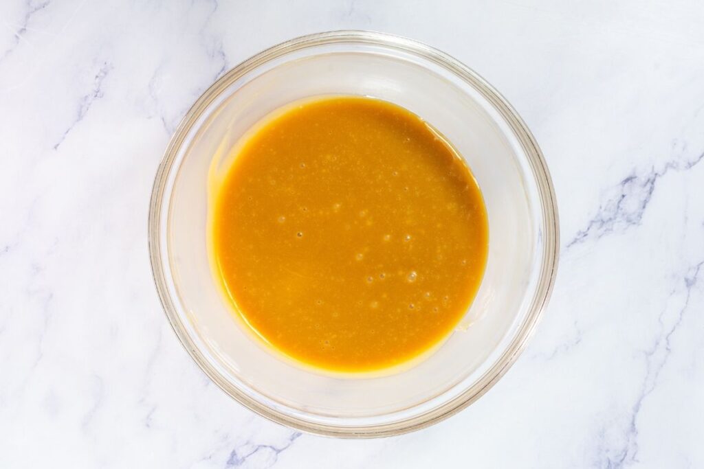 A glass bowl filled with a smooth, golden-yellow liquid sits on a white marble surface.