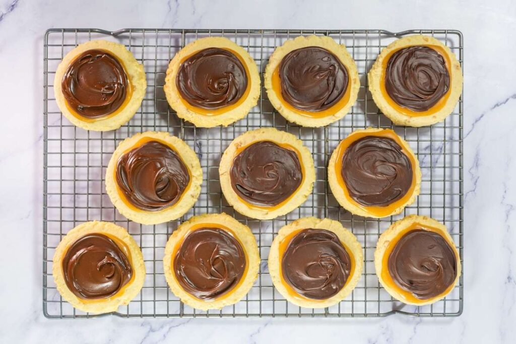 Twelve round cookies topped with swirled chocolate icing are arranged on a cooling rack over a marble surface.