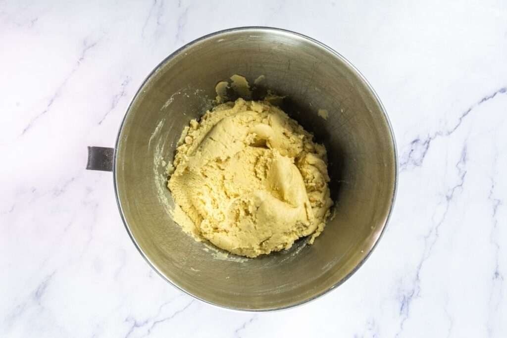 A metal mixing bowl filled with raw cookie dough sits on a white marble surface.