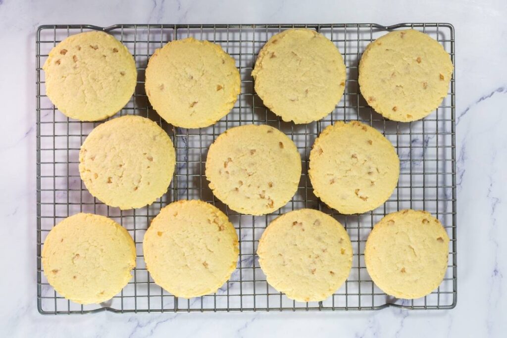 Twelve round shortbread cookies cooling on a wire rack atop a marble surface.