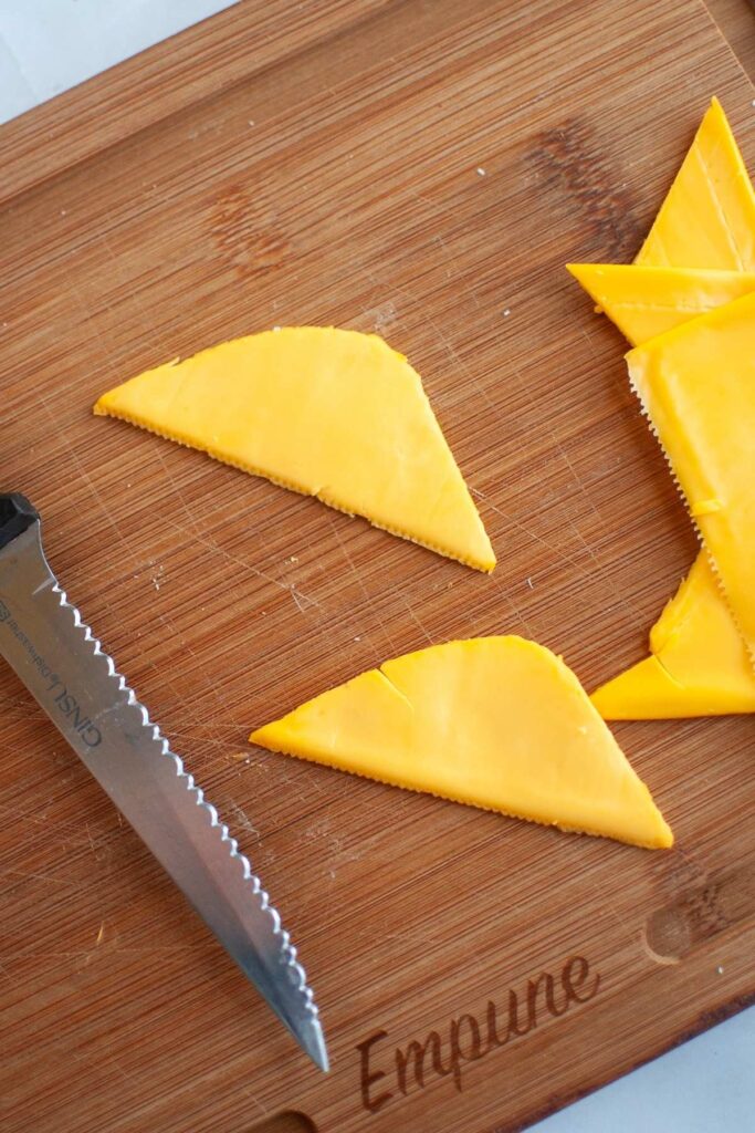 Serrated knife and triangular slices of yellow cheese on a wooden cutting board labeled "Empune.