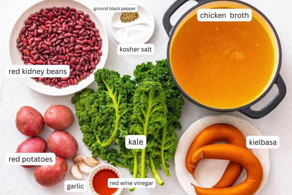 Ingredients for a soup: red kidney beans, red potatoes, garlic, kale, red wine vinegar, kosher salt, ground black pepper, chicken broth, and kielbasa sausage.