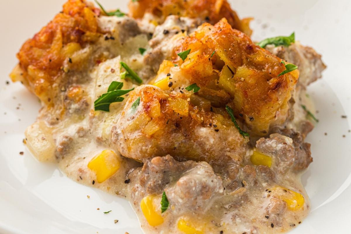 A serving of tater tot casserole with ground beef, creamy sauce, corn, and herbs, garnished with black pepper and parsley on a white plate.