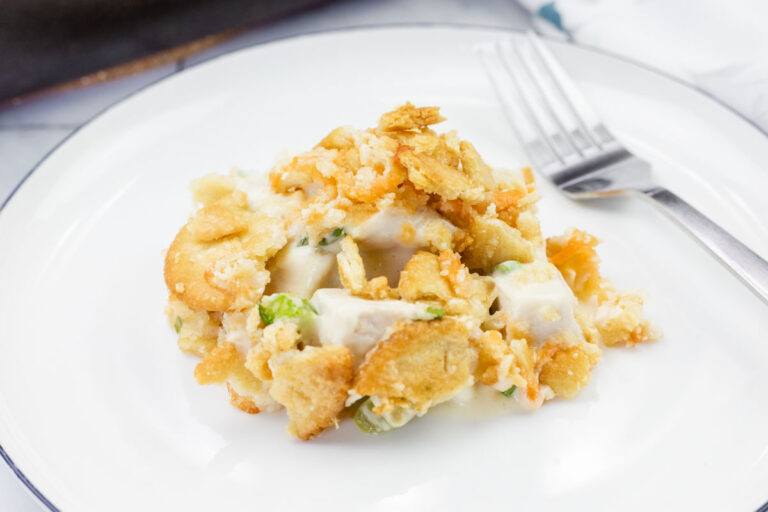 A serving of chicken casserole with cracker topping on a white plate, accompanied by a fork.