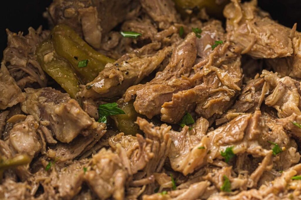 Close-up of shredded cooked meat mixed with sliced green peppers and garnished with small pieces of parsley.