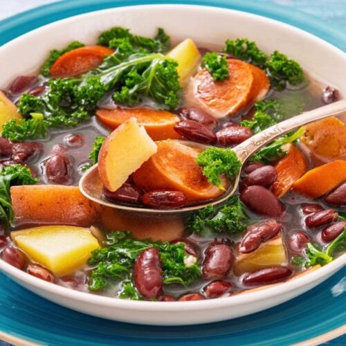 A bowl of Sausage & Kale Soup, served with a spoon on a blue-rimmed plate.