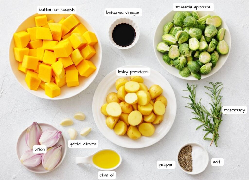 Assorted raw ingredients including butternut squash, brussels sprouts, baby potatoes, shallot, garlic, rosemary, balsamic vinegar, olive oil, salt, and pepper on a white background.