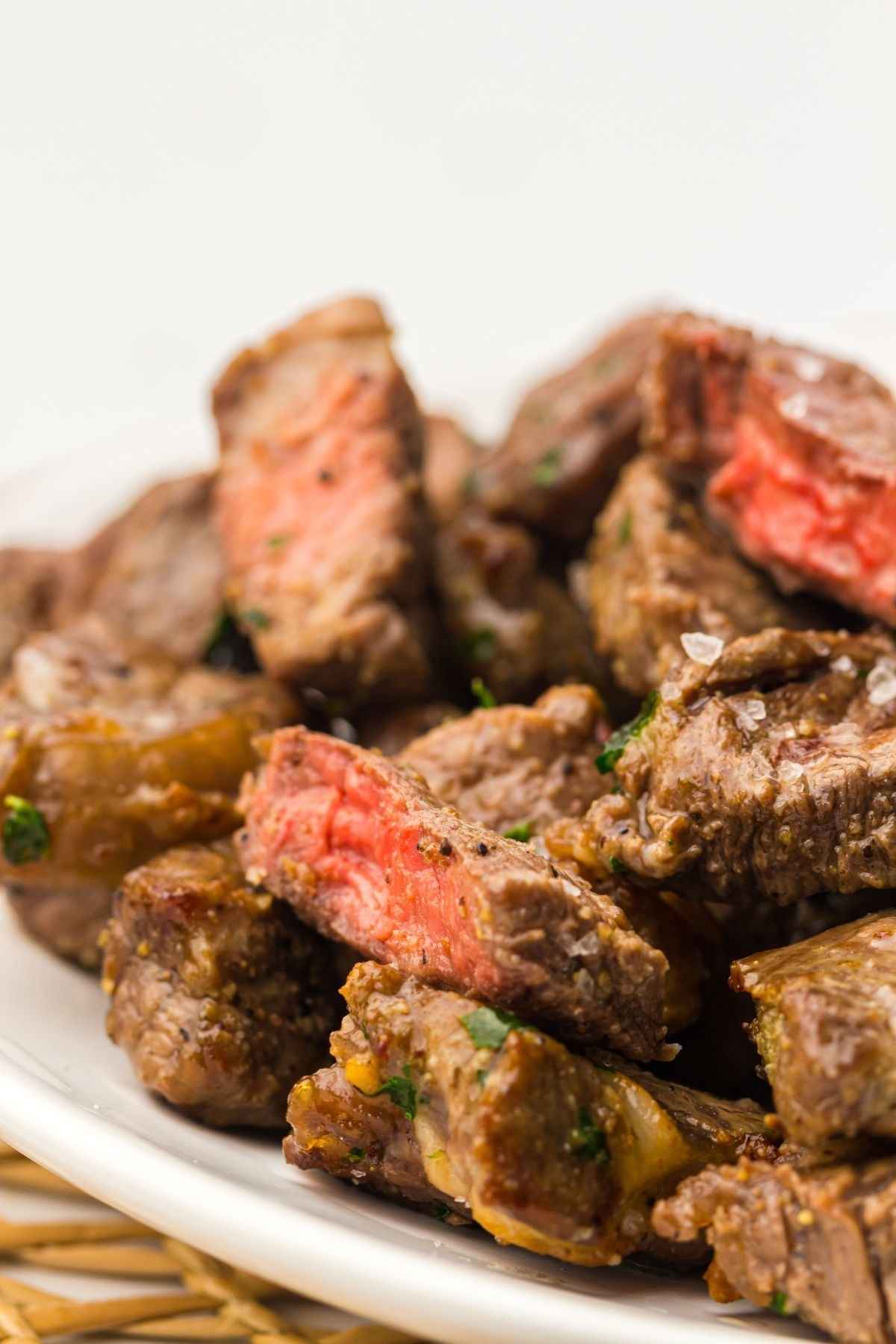 A plate of cooked steak bites, some pieces showing a pink center, indicating medium-rare doneness, on a white dish.
