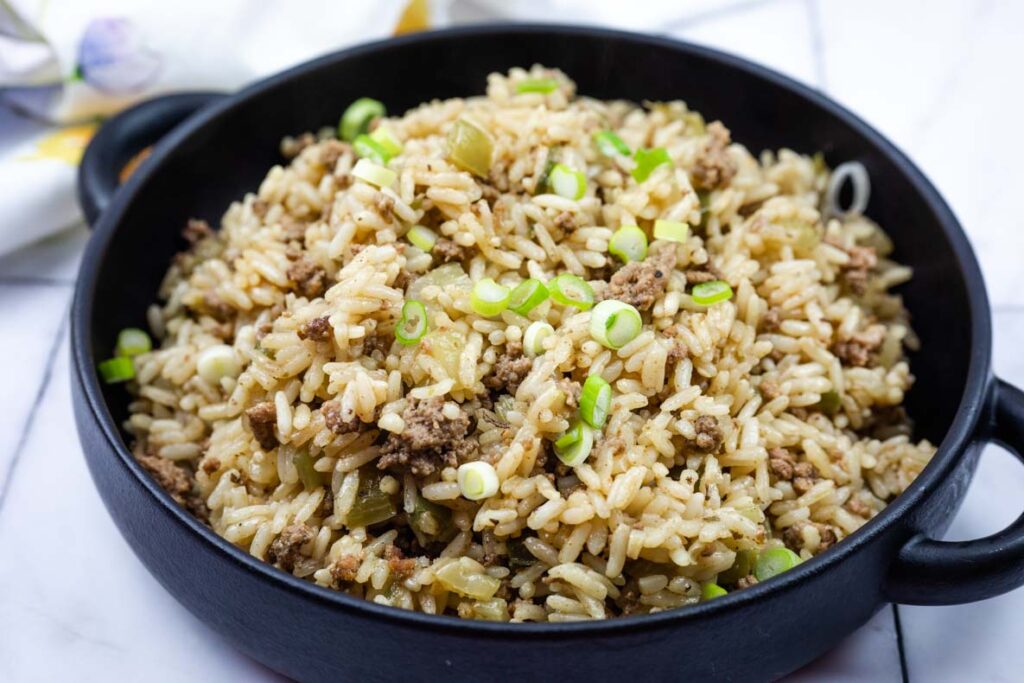 A black bowl filled with cooked rice mixed with ground meat, diced vegetables, and topped with sliced green onions.