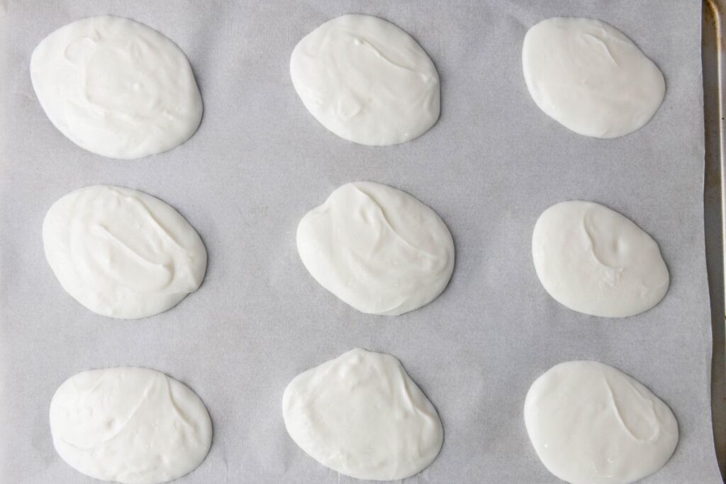 Nine dollops of yogurt are spaced out on a baking sheet lined with parchment paper.