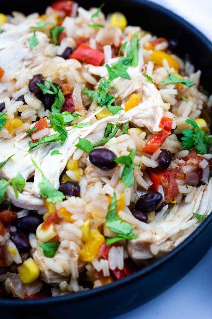 A close-up of a bowl filled with rice, shredded chicken, black beans, corn, diced tomatoes, and chopped cilantro.