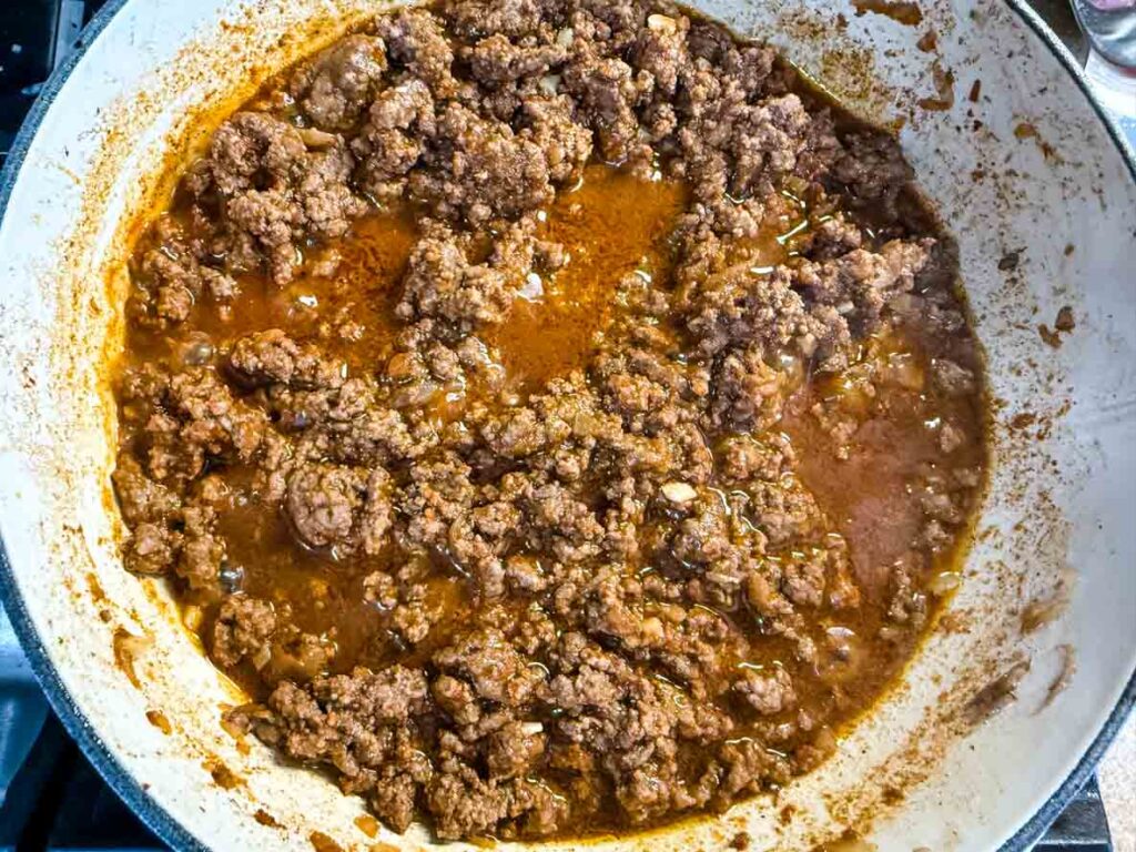 Cooked ground beef in a skillet with visible juices and seasonings.