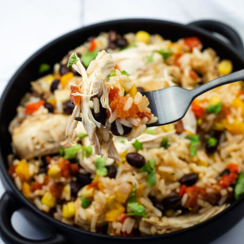 A close-up of a fork holding a bite of Slow Cooker Santa Fe Chicken over a bowl with the same mixed dish.