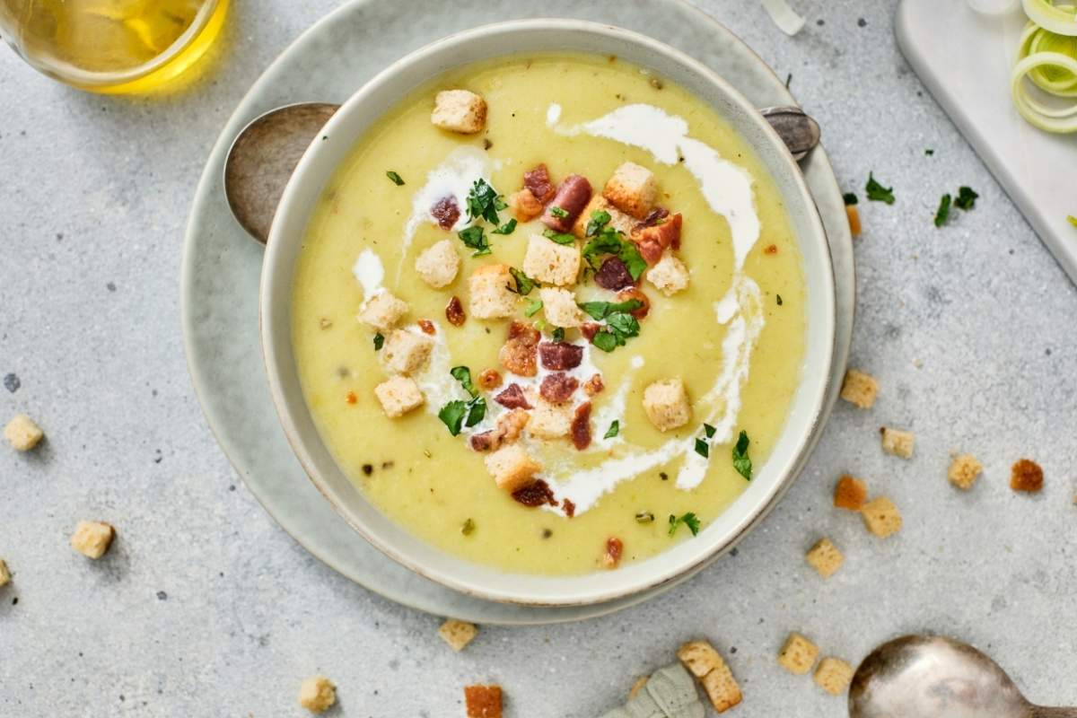 A bowl of Gordon Ramsay's Leek & Potato Soup is placed on a plate with a spoon nearby.