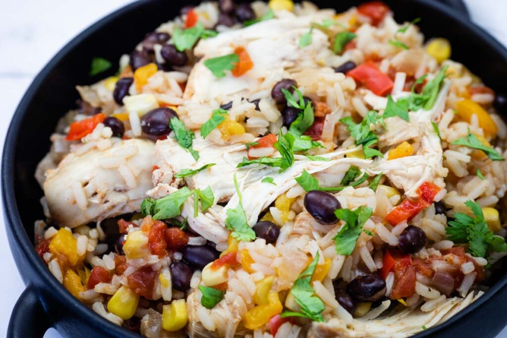 A bowl of Slow Cooker Santa Fe Chicken mixed with shredded chicken, black beans, corn, diced tomatoes, bell peppers, and chopped cilantro.