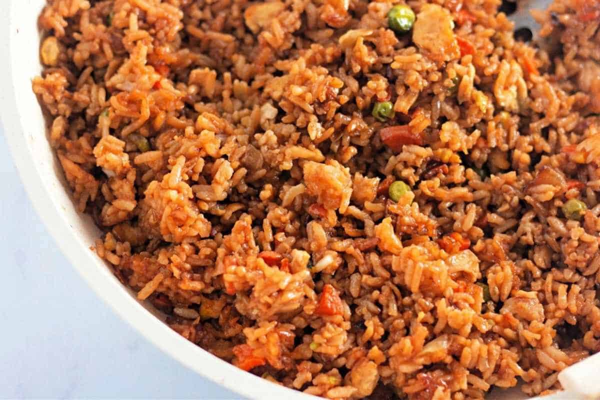 A close-up of a plate of fried rice mixed with vegetables, small pieces of meat, and a savory brown sauce.