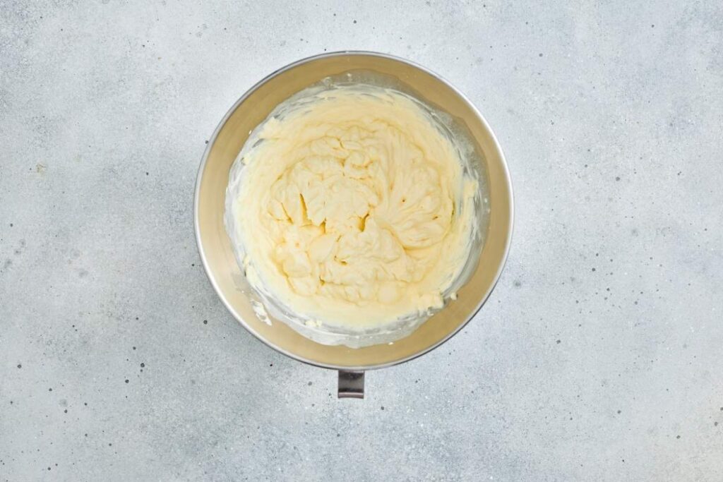 A metal mixing bowl filled with whipped butter on a light gray textured surface.