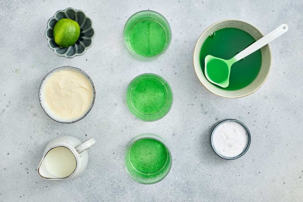 A group of glasses with green liquid and a lime in a bowl.