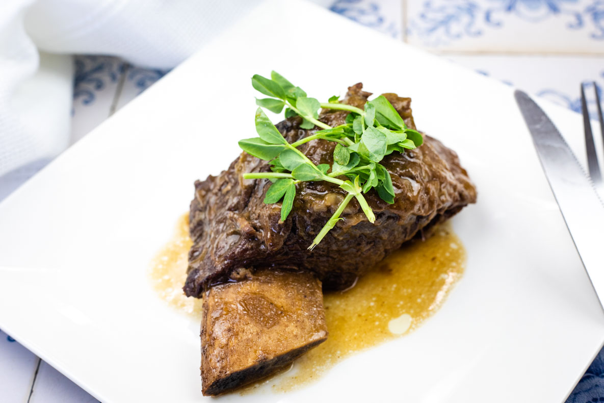 A Guinness-Braised Beef Short Ribs, garnished with parsley, served on a white square plate.