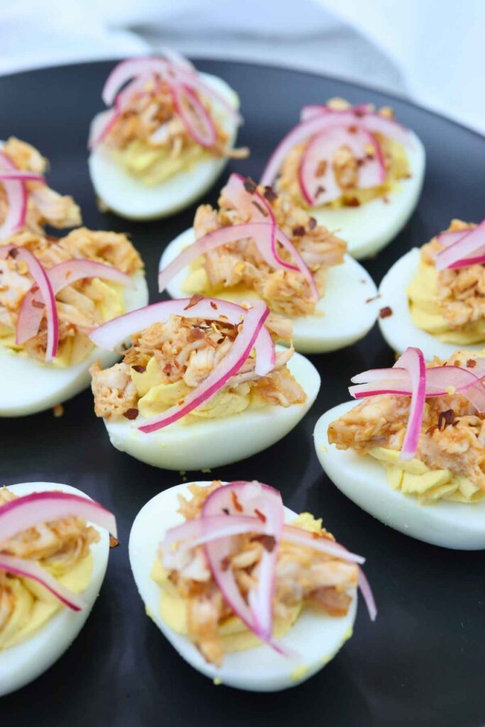 Deviled eggs topped with shredded tuna and thinly sliced red onions, arranged on a black plate.