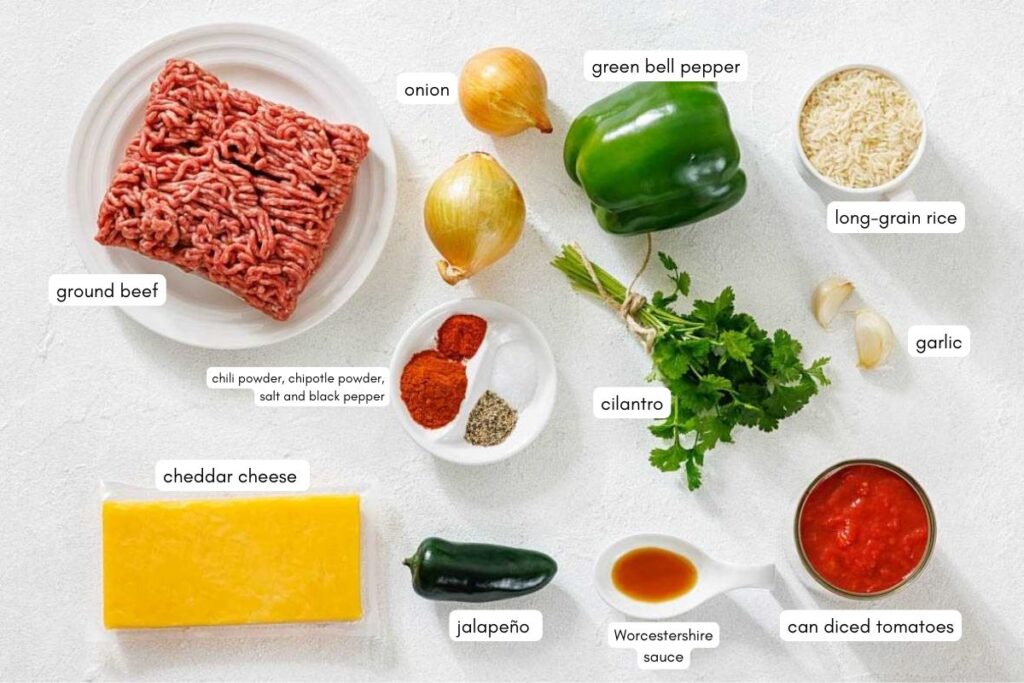 Ground beef, cheddar cheese, jalape&ntilde;o, onions, green bell pepper, cilantro, long-grain rice, garlic, canned diced tomatoes, Worcestershire sauce, and spices arranged on a white surface.