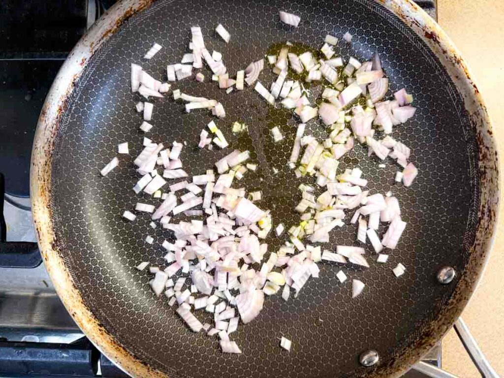 Diced onions are being sautéed in oil in a frying pan on a stovetop.
