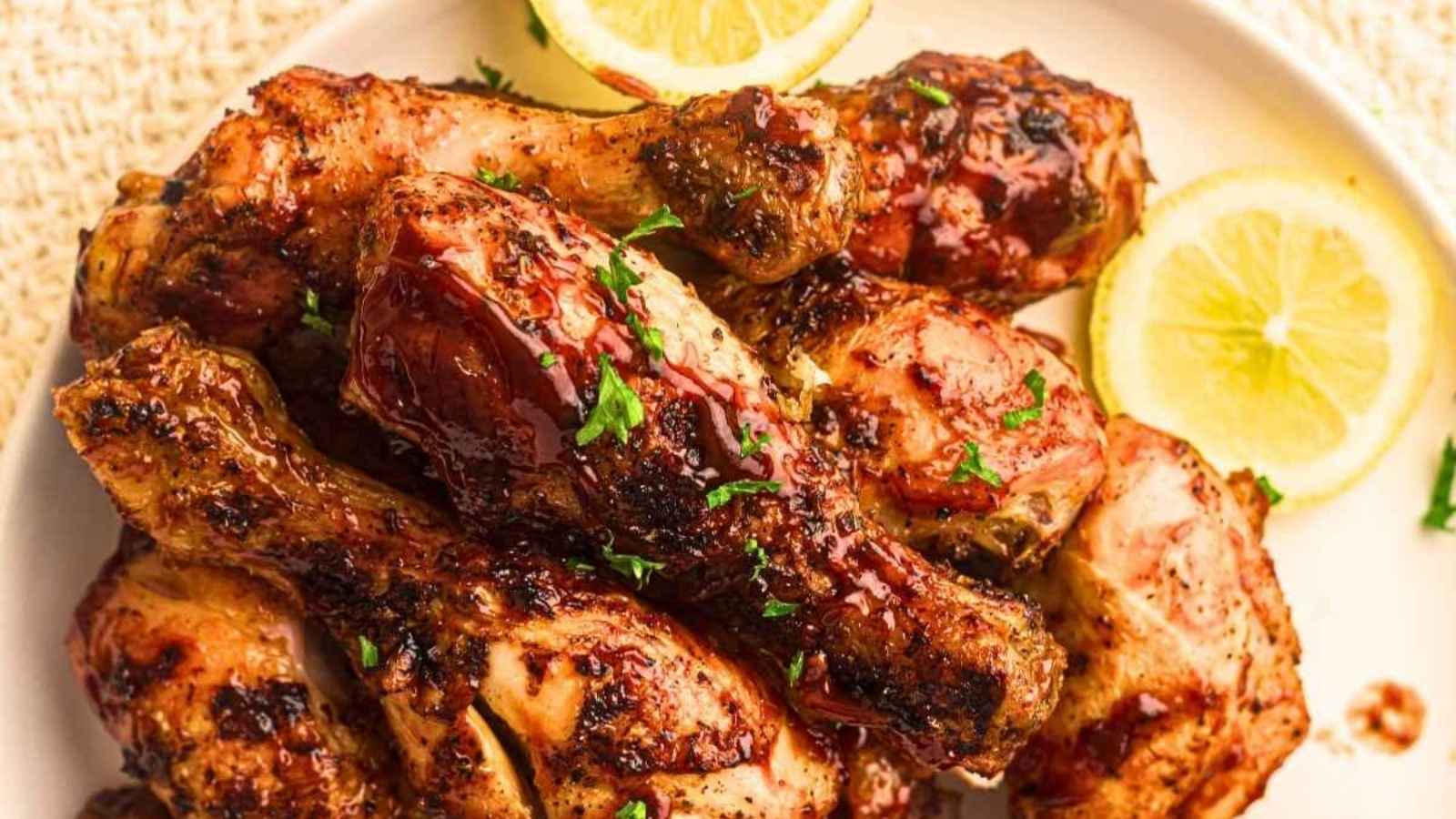 A plate of grilled chicken drumsticks garnished with chopped herbs, served with lemon slices.