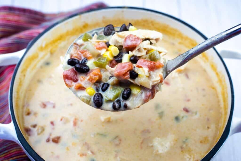 A ladle of creamy Chicken Tortilla  soup with black beans, corn, tomatoes, green peppers, and shredded chicken held over a pot.