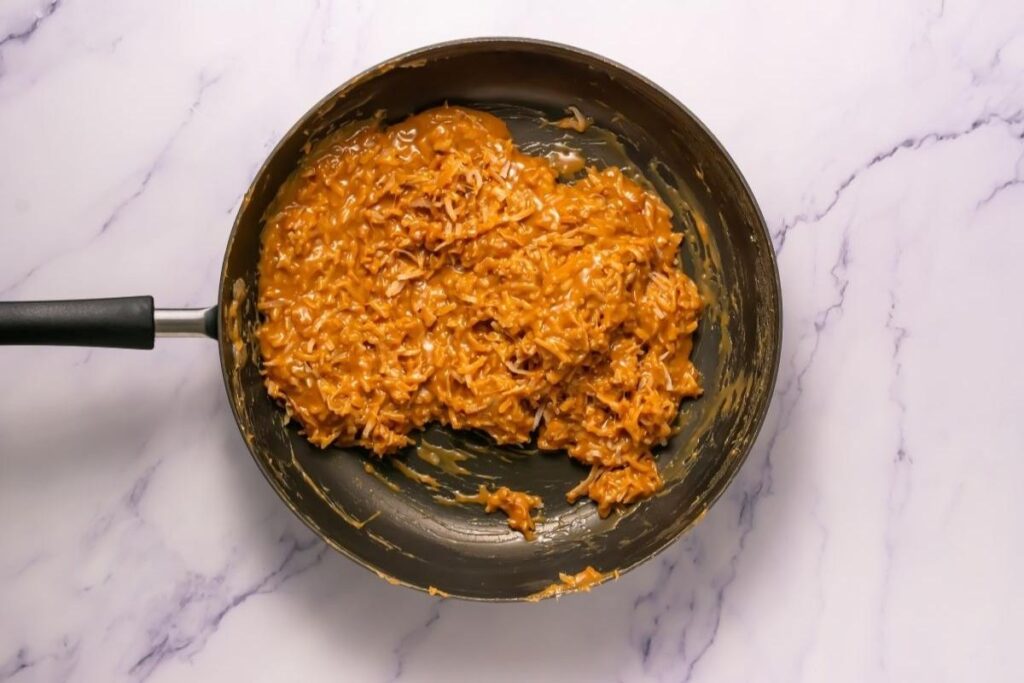A skillet filled with a thick, orange-brown mixture, likely cooked noodles or pasta in sauce, sits on a white marble surface.