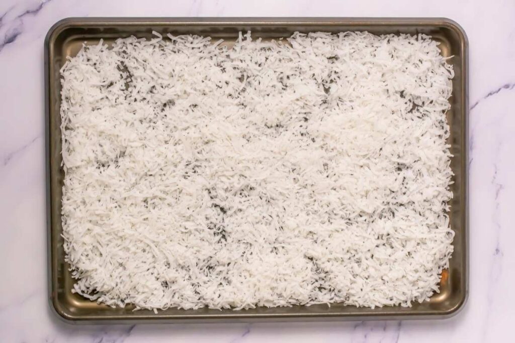 A baking sheet covered with an even layer of shredded coconut on a marble surface.