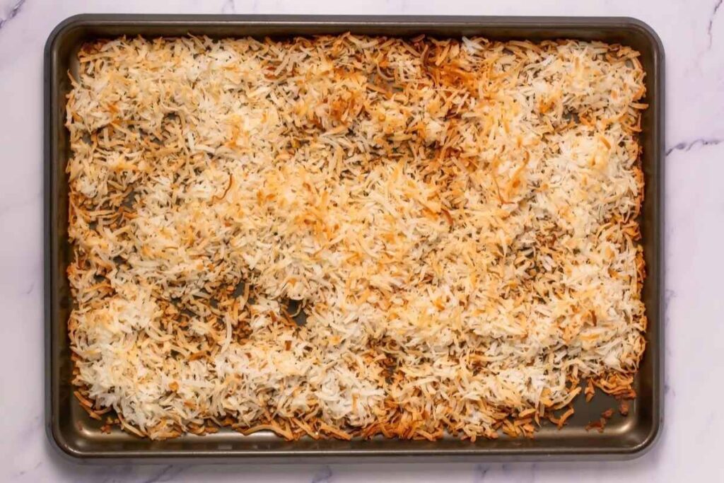 A baking sheet with shredded coconut toasted to a mix of golden brown and white on a marble surface.