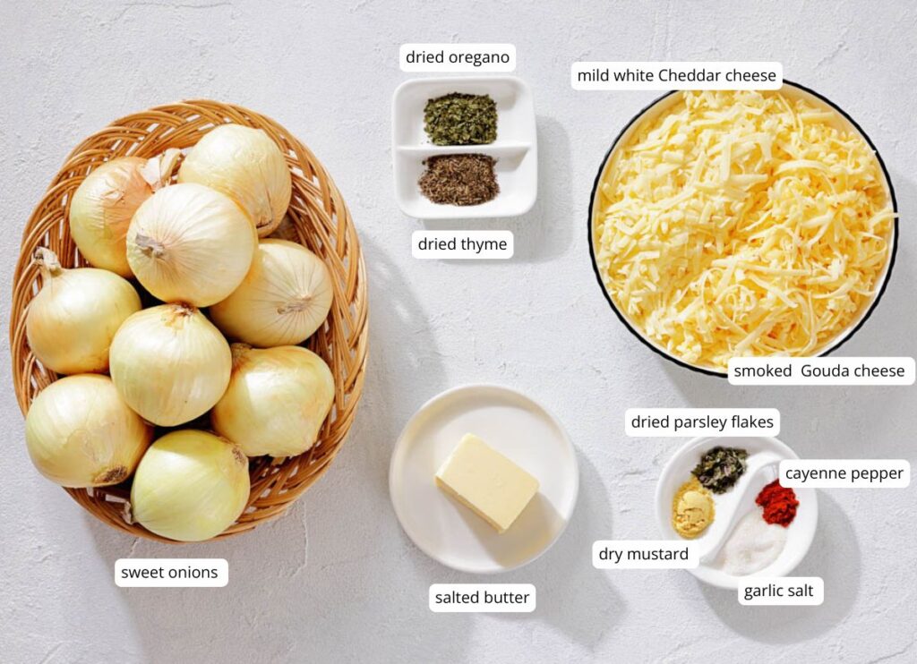 A basket of sweet onions, grated cheeses, salted butter, and small plates of dried herbs and spices arranged on a white surface.
