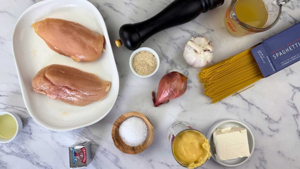 Raw chicken breasts, dry spaghetti, garlic, shallot, cream cheese, canned artichokes, chicken broth, pepper grinder, salt, oil, and breadcrumbs are arranged on a marble countertop.